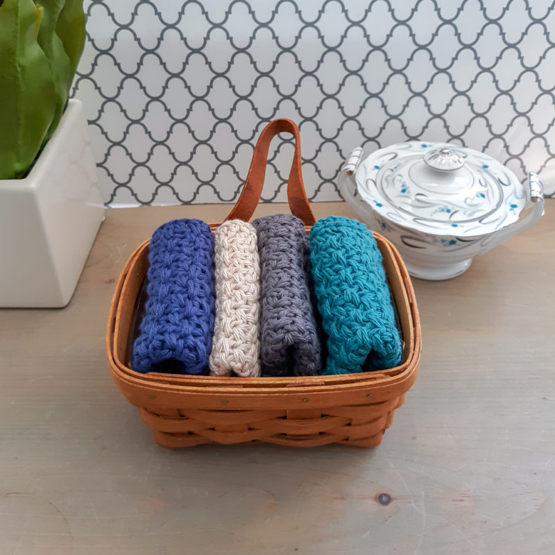 Four Crochet dishcloths in basket with flower accent and ceramic bowl accent