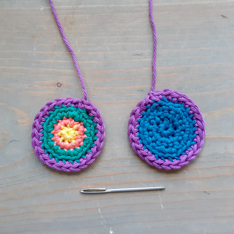 two crochet rounds and darning needs on neutral wood background
