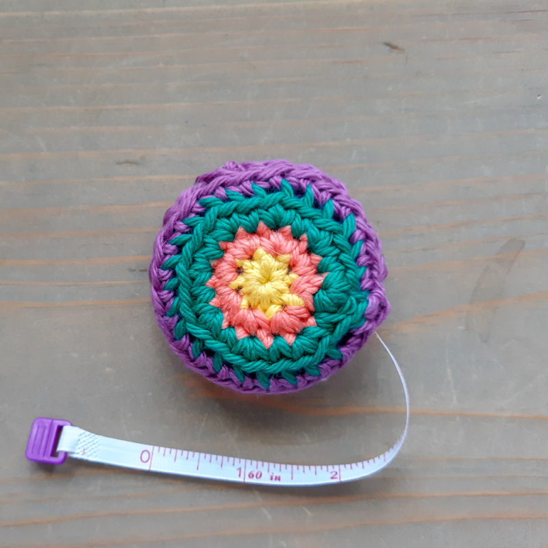 Crochet Tape Measure with 3 inches of tape out on neutral wood backgound