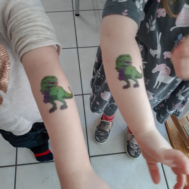 Picture of kids' arms with a temporary tattoo of a t-rex knitting