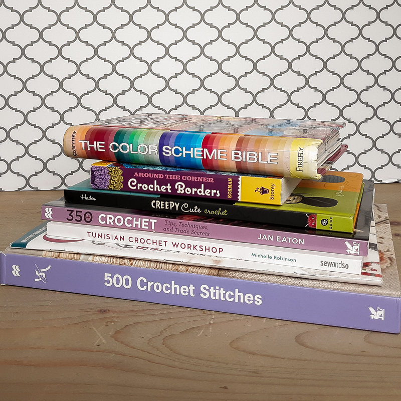 Stack of crochet stitch books on a neutral wood table