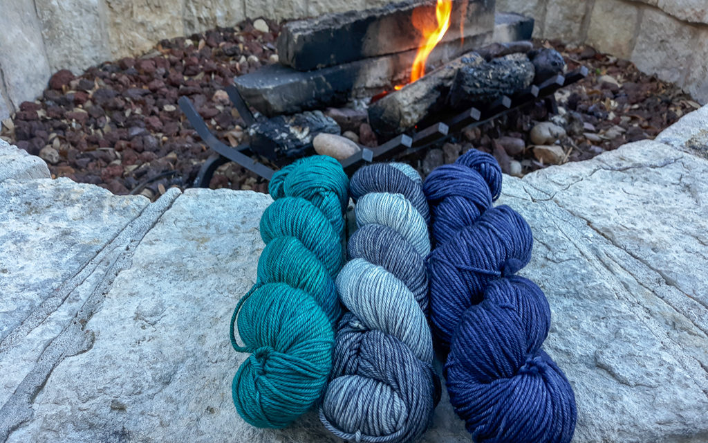 3 hanks of yarn displayed on stone with a firepit in the background